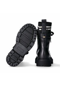 Stivali alla caviglia in pelle nera con suola in gomma texture. Presentano un risvolto a maglia con strisce bianche e una linguetta sul retro.