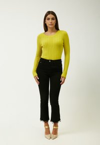Maglione giallo a coste con maniche lunghe, abbinato a jeans neri a vita alta con orlo in pizzo. Indossato con tacchi scintillanti argento.