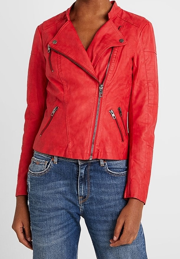 Giacca da moto in pelle rossa con un design aderente, zip asimmetrica e numerose tasche con zip. Indossata sopra jeans blu.