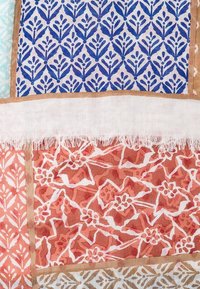Tissu à motifs multiples présentant des dessins floraux bleus sur fond blanc, des motifs abstraits corail et orange, des bords frangés et des bordures beige.