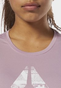 Světle fialové sportovní tričko s kulatým výstřihem a strukturovaným grafickým vzorem v bílé na přední části. Hladká tkanina, krátké rukávy.