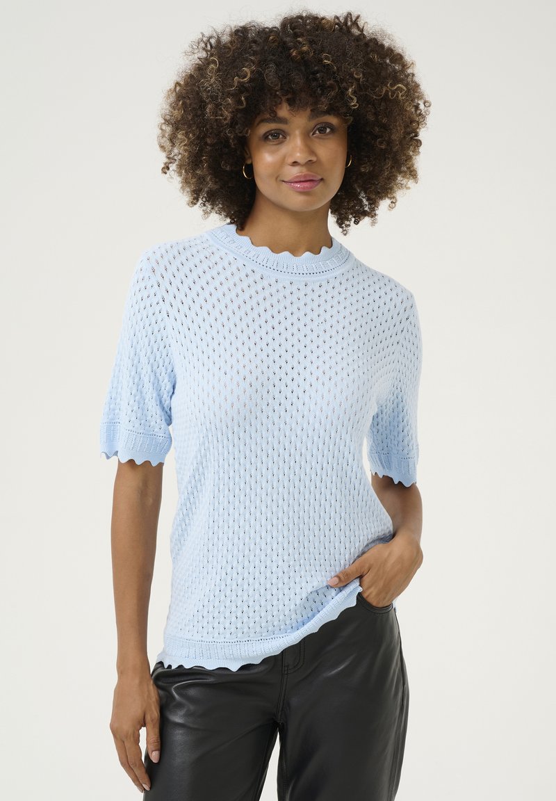 Šviesiai mėlynas megztukas su trumpomis rankovėmis, su banginiu apykakle ir apatine dalimi, turintis tekstūruotą atvirą raštą. Derinamas su juodais odiniais kelnėmis.