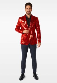 Rote, mit Pailletten besetzte Blazerjacke mit tailliertem Schnitt und Reverskragen, getragen über einem schwarzen Hemd. Kombiniert mit dunkel gemusterten Hosen und schwarzen Schuhen.