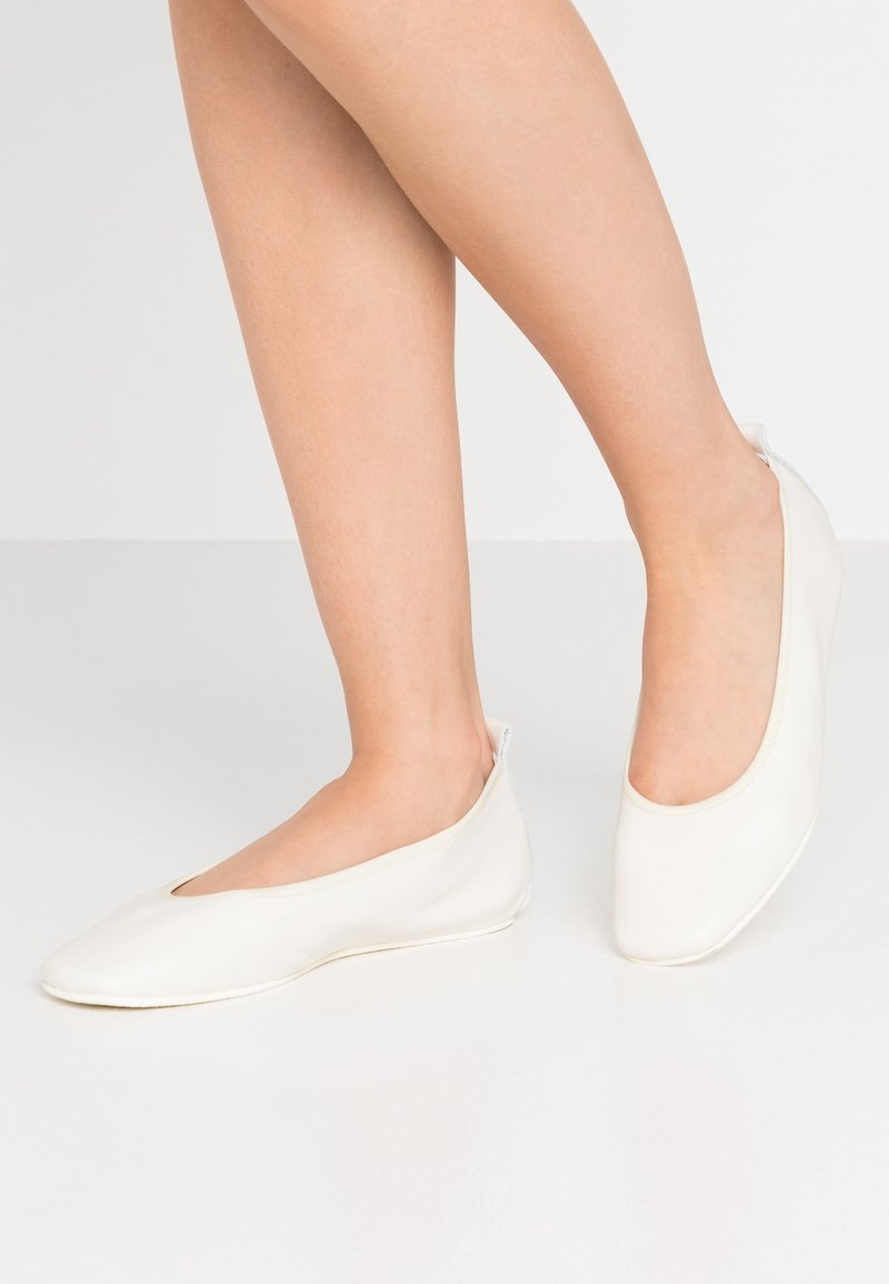 Vita läderballerina med rund tå, platt sula och låg snittdesign, som har en slät textur och en minimalistisk accent.