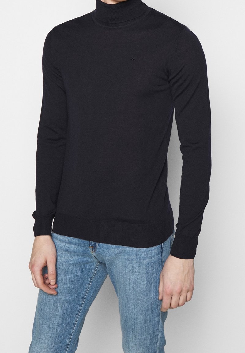 Maglione dolcevita nero con maniche lunghe, tessuto morbido, design aderente e polsini e orlo a coste, abbinato a jeans denim azzurri.