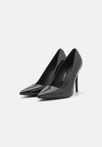 Zwarte gepatenteerde leren hoge hakken met een spitse neus, slank ontwerp en een slanke stilettohak. Het interieur is voorzien van een gladde zwarte voering.