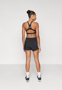 Čierna športová podprsenka s dizajnom racerback a detailom loga, v kombinácii s čiernymi šortkami s voľným strihom a elastickým pásom.
