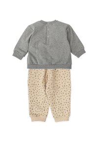 Sudadera gris con botones a presión en el cuello y joggers beige de estampado con pequeños cuadrados y puños acanalados.