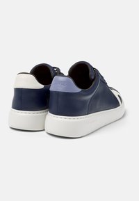 Pair of navy blue leather sneakers with thick white soles, featuring white and light blue heel patches, angled rear view on white background.