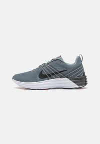 Sivé športové topánky s textúrovan�ým zvrškom, čiernym logom swoosh, kontrastnou bielou medzipodrážkou a červenými akcentmi na päte.