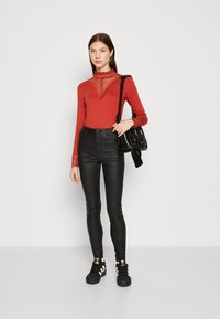 Rød langermet topp med blonde detaljer ved halsen, kombinert med svarte skinny bukser og svarte joggesko med gullasjoner. Bærer en svart veske.