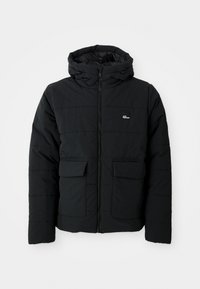 Veste matelassée noire avec capuche, fermeture éclair à l'avant, deux grandes poches à rabat et petit logo blanc sur la poitrine.