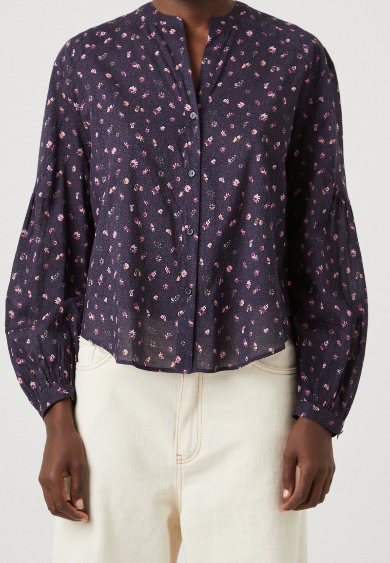 Blouse marine boutonnée avec imprimé floral ; manches longues bouffantes et col montant ; tissu doux et léger avec une coupe décontractée.