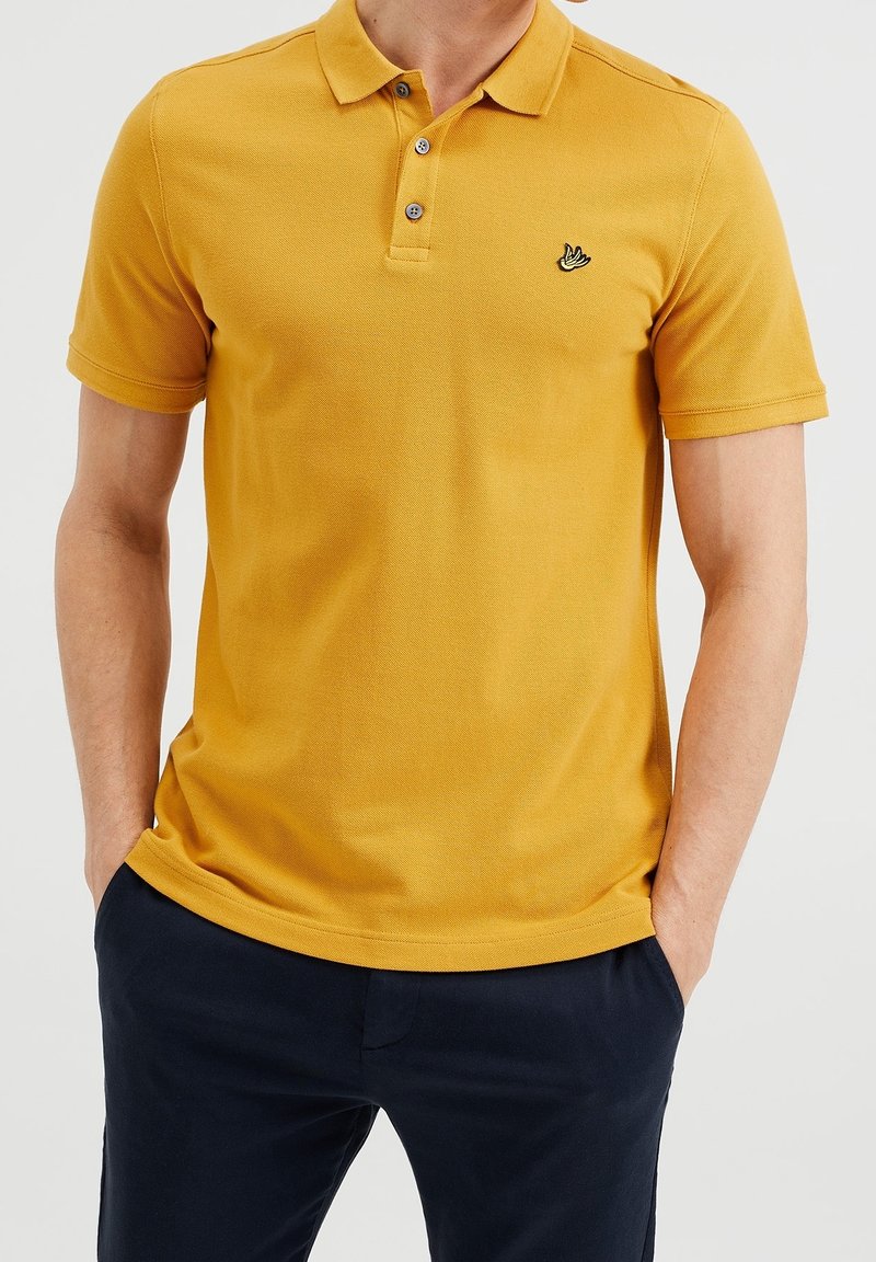 Senapsgul polo t-shirt med en texturerad yta, treknappsstängning och en liten svart broderad logotyp på bröstet.