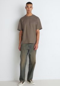 Brun kortærmet T-shirt parret med lys grønne jeans og beige sneakers, med en afslappet pasform og enkelt design.