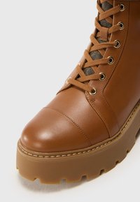 Gros plan d'une botte en cuir marron à lacets, avec une semelle en caoutchouc épaisse et des détails cousus sur l'avant et les côtés.