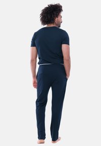Marineblå kortærmet skjorte og matchende bukser lavet af blødt stof. Bukserne har elastisk talje. Barfodsbillede set fra bagsiden.
