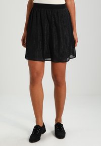 Černá krátká sukně z lehkého, texturovaného materiálu. Obsahuje pružný pas a průhledné vrstvy, které vytvářejí vzdušný siluetu.