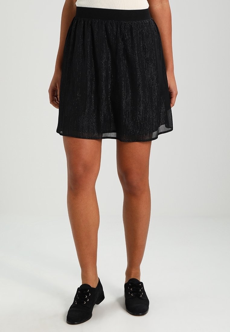 Černá krátká sukně z lehkého, texturovaného materiálu. Obsahuje pružný pas a průhledné vrstvy, které vytvářejí vzdušný siluetu.
