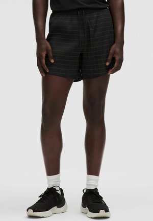 Sort shorts med ternet mønster, letvægtsstof, elastisk talje med snoretræk og en afslappet pasform, parret med sorte sneakers.