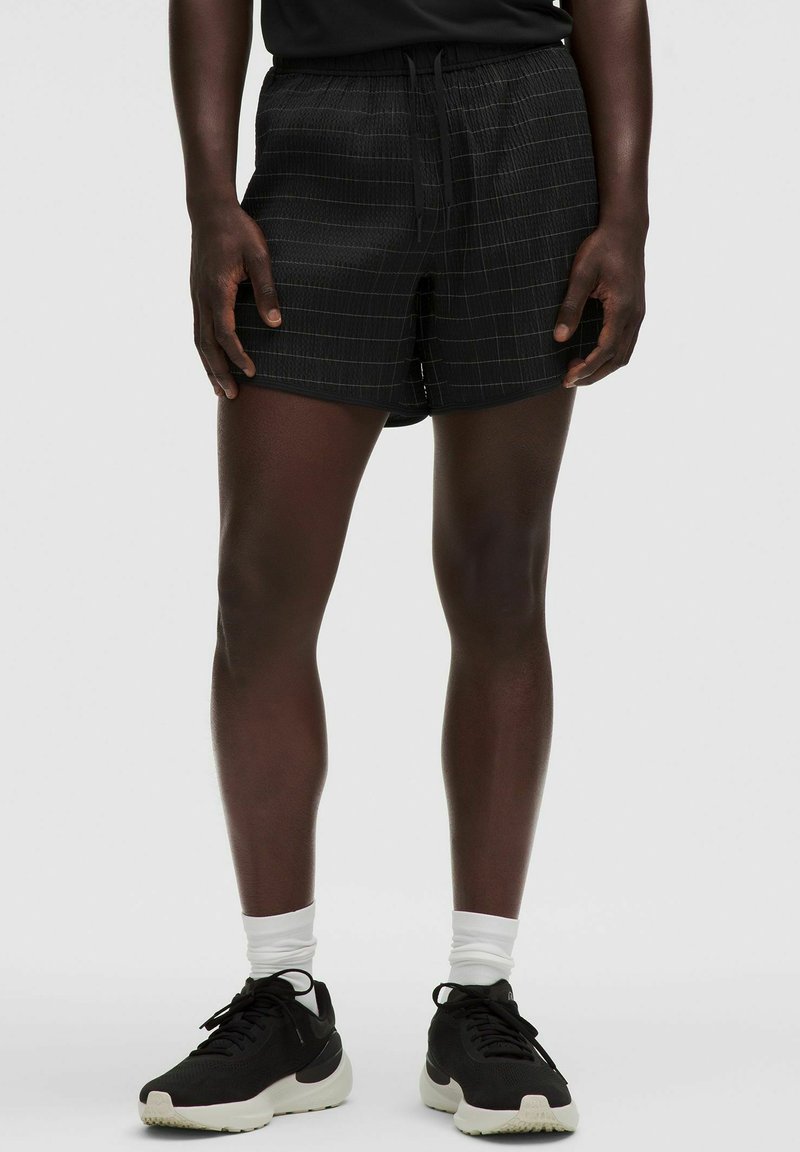Mustat shortsit ruudullisella kuviolla, kevyttä kangasta, joustava vyötärönyöri, rento leikkaus, yhdistetty mustiin lenkkareihin.