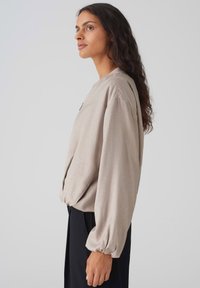 Lichtbeige lange mouw top met een ontspannen pasvorm, textuurstof, gegatherde ballonmouwen en een ronde halslijn, gecombineerd met donkere broek.