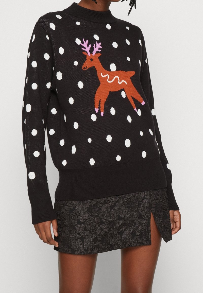 Maglione nero con pois bianchi e un design di renna marrone, con dettagli rosa e scollo rotondo. Indossato con una gonna nera testurizzata.