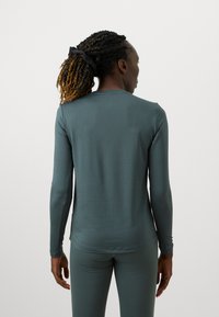 Dlhý rukáv, priliehavý top v tlmenej teal farbe. Hladká textúra s jednoduchým dizajnom a okrúhlym výstrihom, doplnený o zodpovedajúce priliehavé nohavice.