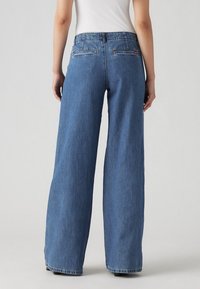 Vida-blå denimjeans med vida ben och hög midja, bakfickor samt råa fållar. Tyget verkar robust med en lätt blekt finish.