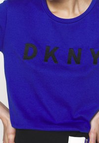 Niebieska bawełniana koszulka z okrągłym dekoltem i wyraźnym czarnym napisem "DKNY" na piersi. Gładka tekstura z dopasowanym krojem.