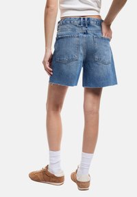 Vaaleansiniset farkkushortsit, joissa on revitty helma, kaksi takataskua ja korkea vyötärö. Yhdistetty ruskeisiin tennareihin ja valkoisiin sukkiin.