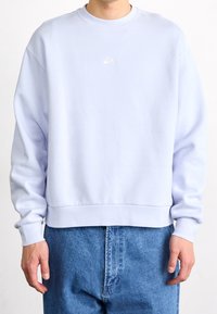 Light blue sweatshirt with a crew neck and ribbed cuffs. Features a small white Nike logo on the chest. Made from soft fabric.