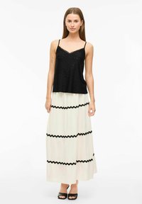 Top de tirantes con encaje negro combinado con una falda larga blanca con rayas onduladas negras. La modelo lleva puestos unos tacones abiertos negros.