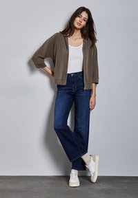 Outfit casual composto da una felpa leggera grigia con zip, una canotta bianca, jeans a gamba larga blu scuro e sneakers bianche con dettagli beige.
