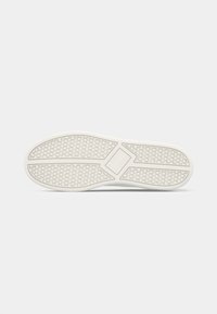 Sole of a white sneaker with circular and rectangular tread patterns, displayed flat against a plain white background.