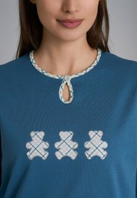 Top in cotone turchese con scollatura a chiave decorativa con bottoni e tre orsetti ricamati in un motivo a quadretti.