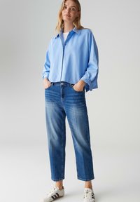 Camicia a bottoni azzurro chiaro, vestibilità comoda; jeans a lavaggio medio con taglio dritto; sneaker bianche con dettagli neri; look casual.