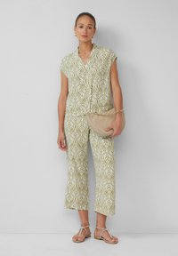 Jasnozielony kombinezon z nadrukiem liści, krótki rękaw, kołnierzyk i ścięte nogawki. Uzupełniony beżową torebką i sandałami na paski.