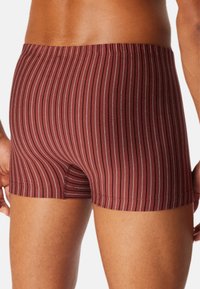 Bordeaux boxers med lodrette hvide og lysegrå striber, tætsiddende design, elastisk talje og glat tekstur. Har en kort benlængde.
