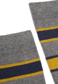 Chaussettes en tricot grises avec des rayures horizontales bleu marine et jaunes près du bord supérieur sur fond blanc.