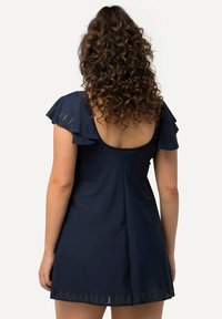 Navy blue uimapuku peittava vaate, jossa on liehuvat hihat ja syvä takaosa. Yhdistä laserleikattu kukkakuviota helman kohdalla. Sujuva kangas.