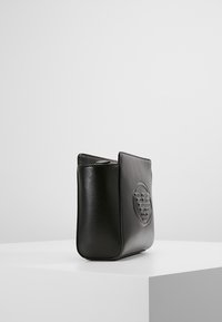 Borsa in pelle nera con una texture liscia, forma rettangolare e un design circolare impresso su un lato. Parte superiore aperta, stile minimalista.