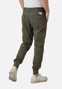 Olijfgroene joggerbroek met een textuurafwerking, elastische tailleband en omgeslagen enkels. Inclusief twee achterzakken en een klein logo-label.