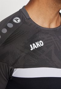 Schwarzes Sporttrikot mit texturierten Mustern, weißen Akzenten und einem auffälligen "JAKO"-Logo auf der Brust und der Schulter.