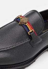 Mocassino in pelle nera con texture a ciottoli, caratterizzato da un accento a strisce arcobaleno e hardware dorato. Design classico con dettagli notevoli.