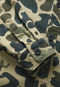 Maglietta con motivo camouflage nei colori verde, beige e blu scuro. Presenta un polsino con bottone, una trama in denim e cuciture a contrasto.