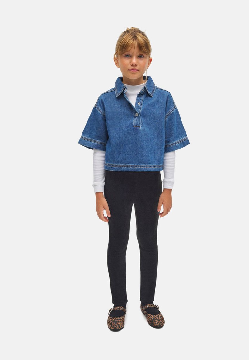 Top de mezclilla corto con mangas cortas, con botonadura; capa blanca de manga larga debajo, combinado con leggings negros y zapatos de estampado de leopardo.