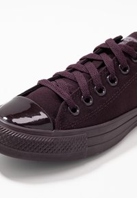 Lila kanvas sneaker med en glansig mörklila tåhuvud, snördesign och mönstrad gummisula med diamantsymmetri.