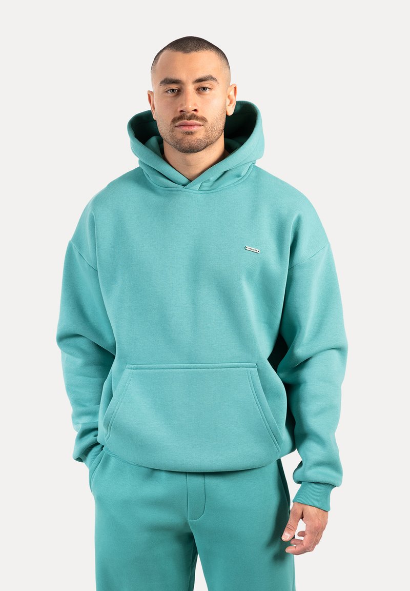 Hoodie turquoise en tissu doux, doté d'une poche avant, d'une capuche à cordon réglable et d'un logo sur la poitrine. Design simple et ample.