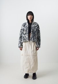 Furry black and white patterned cropped jacket with a zipper and beige long skirt with pockets, paired with black sneakers.
